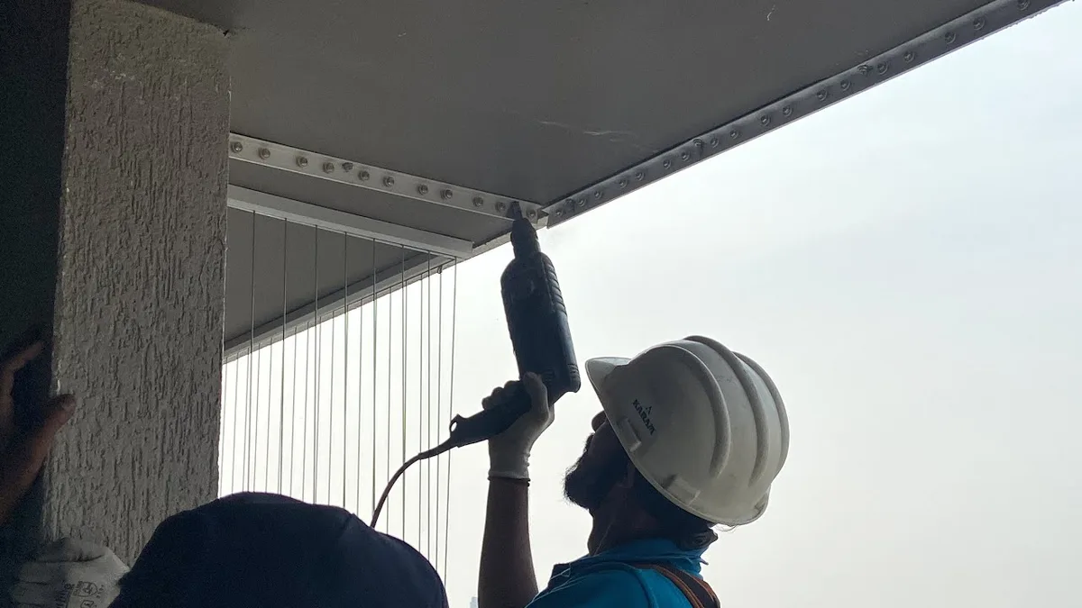 Pemasang profesional sedang mengetatkan kabel invisible grille di tingkat tinggi
