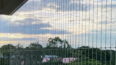 Pandangan dekat kabel invisible grill berlatarkan pokok dan langit, menunjukkan cara ia berfungsi